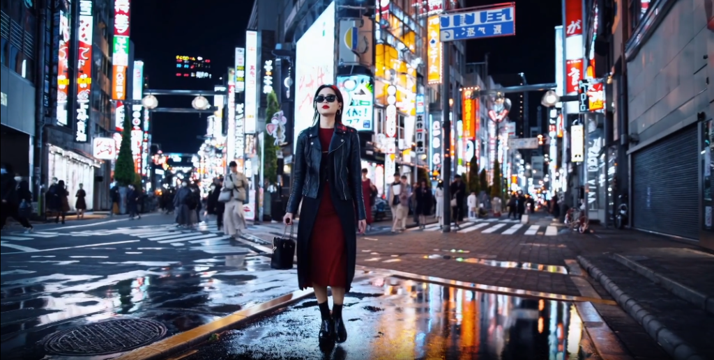 A woman wearing a black coat walking on a wet street at night in Tokyo, Japan. The photo captures the city lights reflecting on the ground as she walks. This image by sora